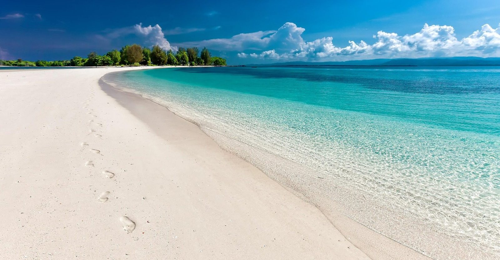 Praia de areia branca com o mar transparente em tons de turquesa e uma ilha arborizada ao fundo